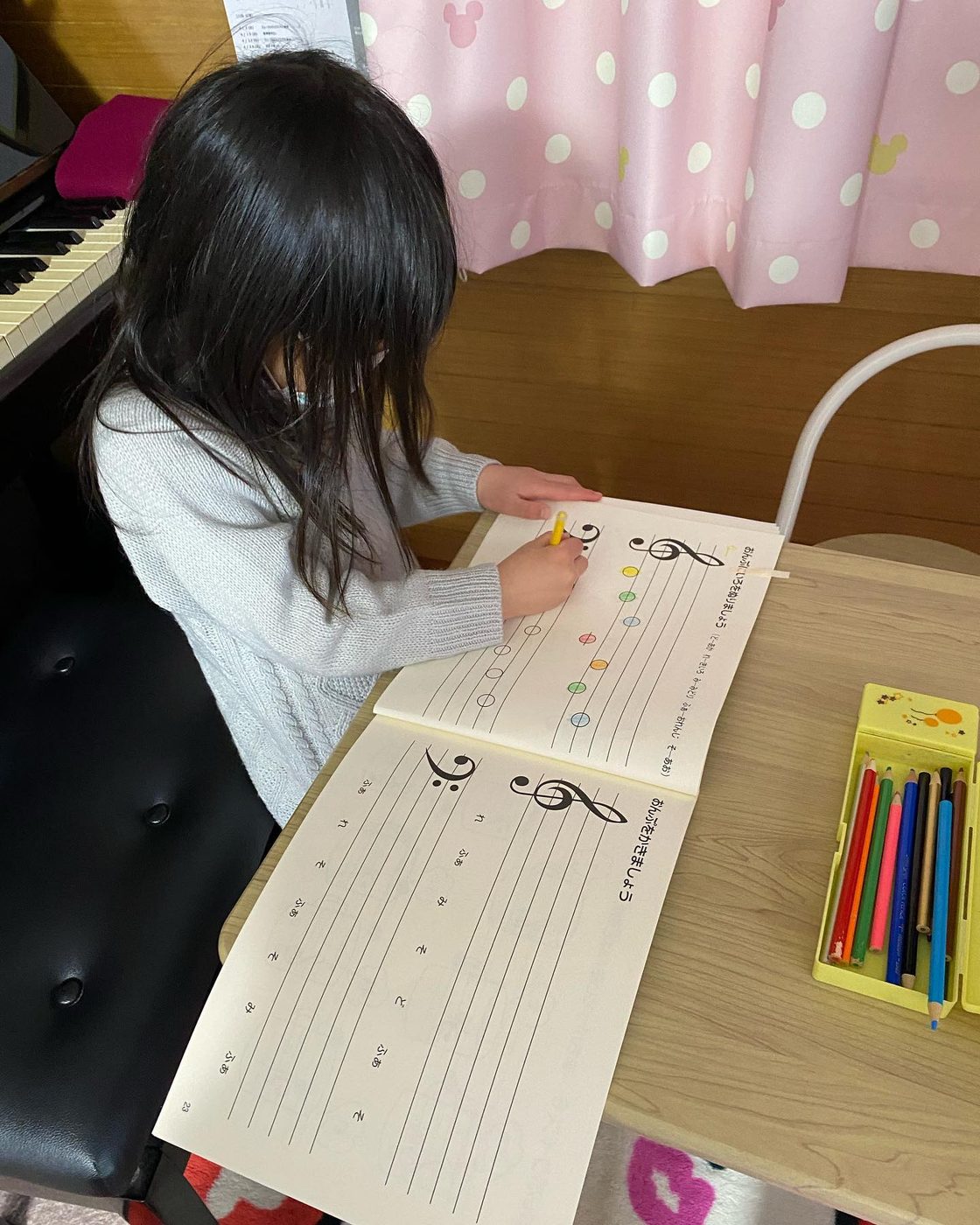 ピアノの前でワークブックに音符を書き込む生徒さん
